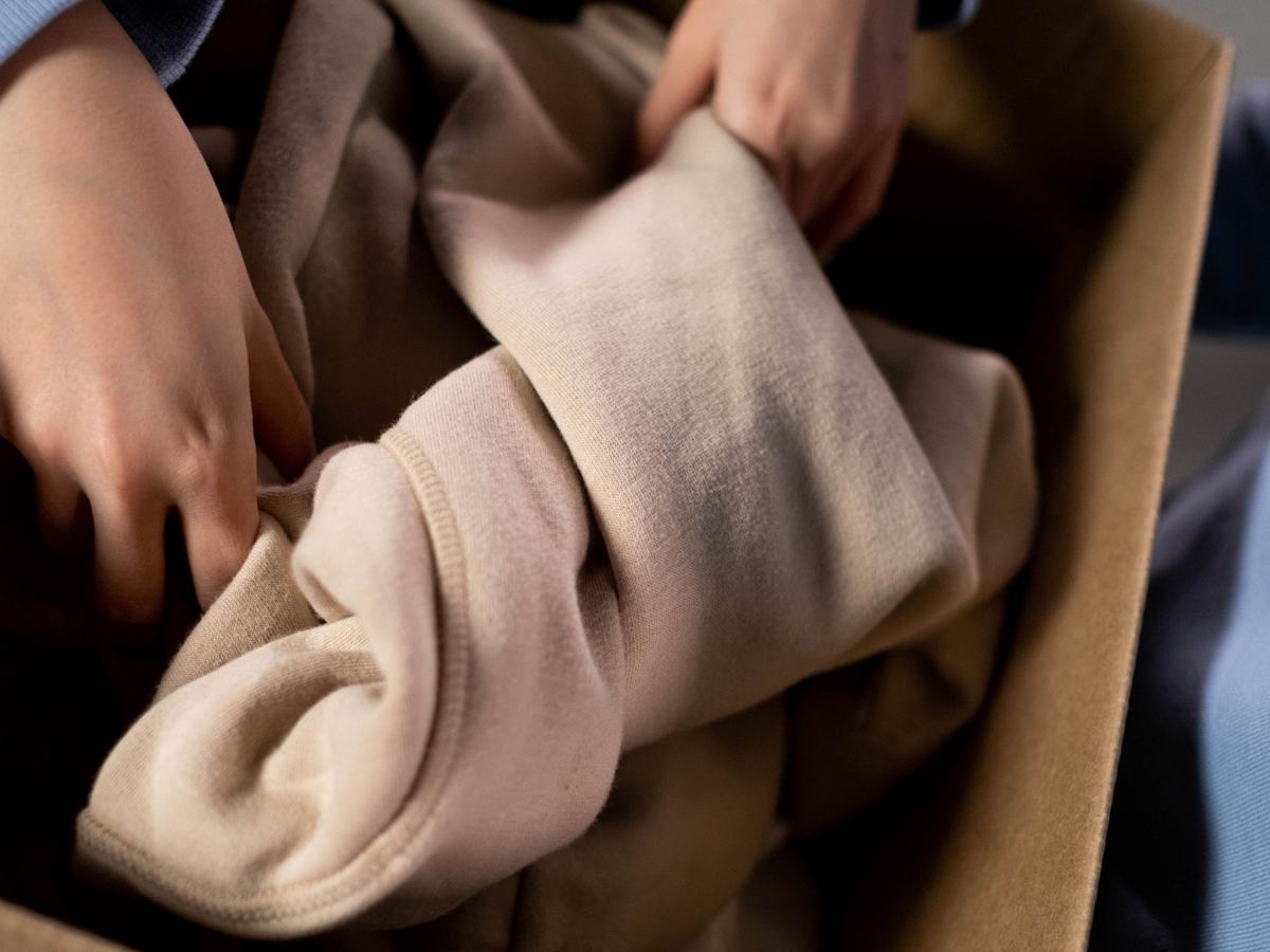 Hände legen ein Kinderoberteil zusammen und packen es in eine Kiste